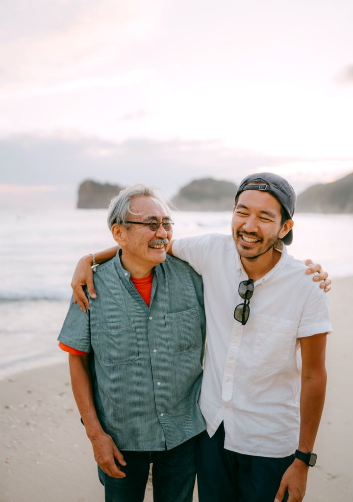 Smiling father and son with arms around each other on the beach